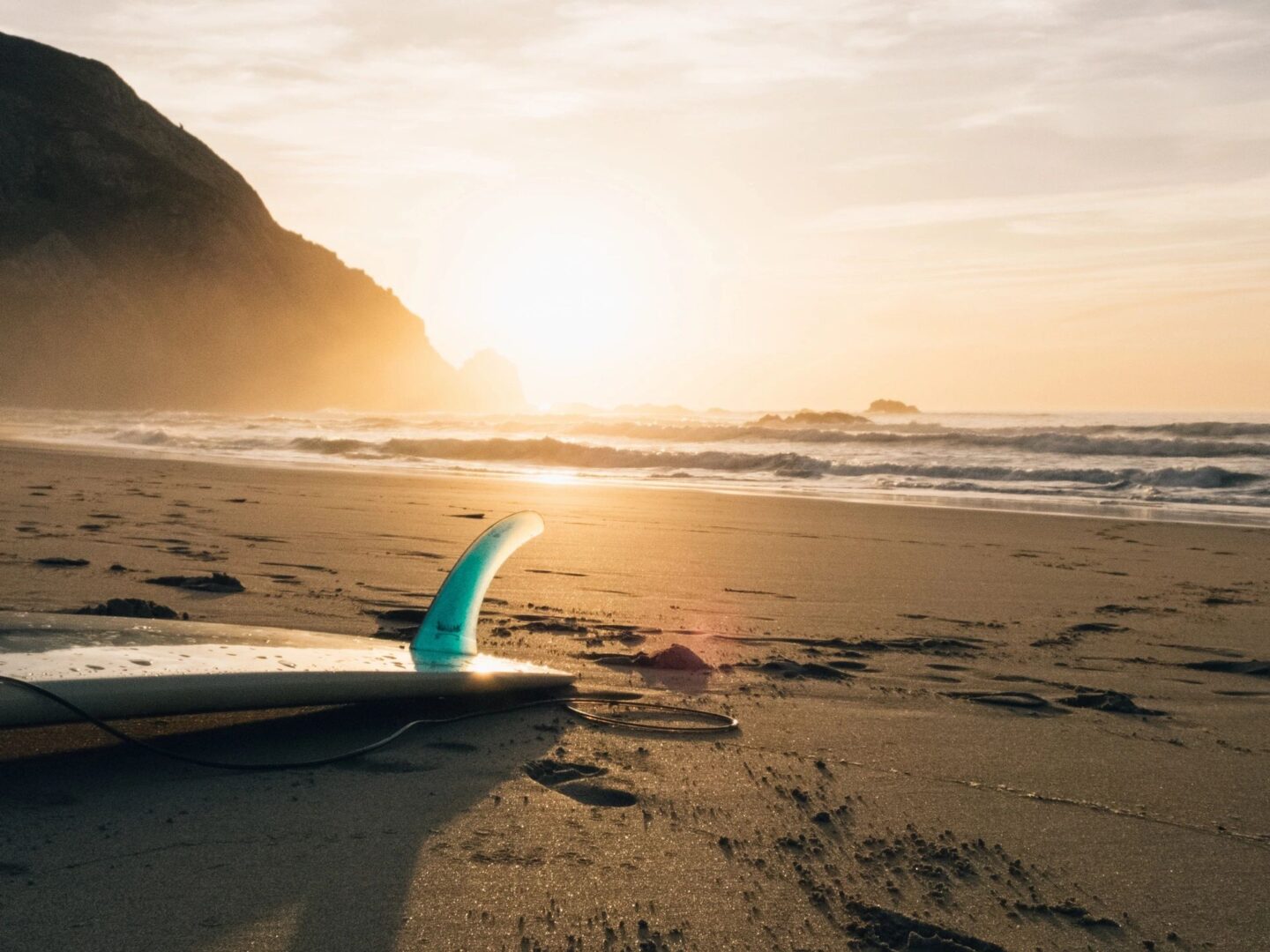 Surfboard resting on sandy beach at sunset.