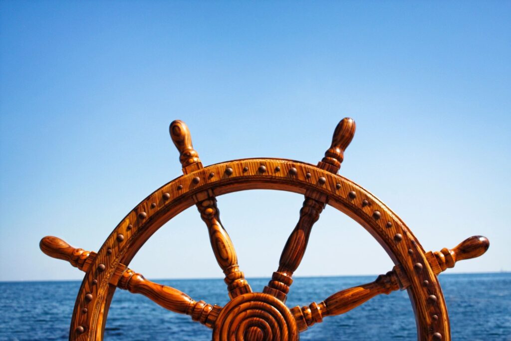 Close-up of a ship's wooden steering wheel against a clear blue sky and ocean.