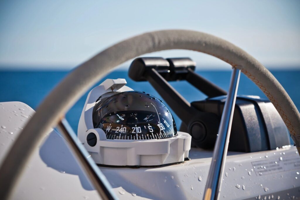 A marine compass on a boat steering wheel with a sea background.