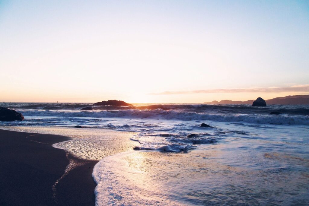 Sunset over ocean waves and sandy beach.