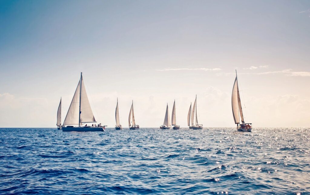 Sailboats on calm ocean under clear sky.
