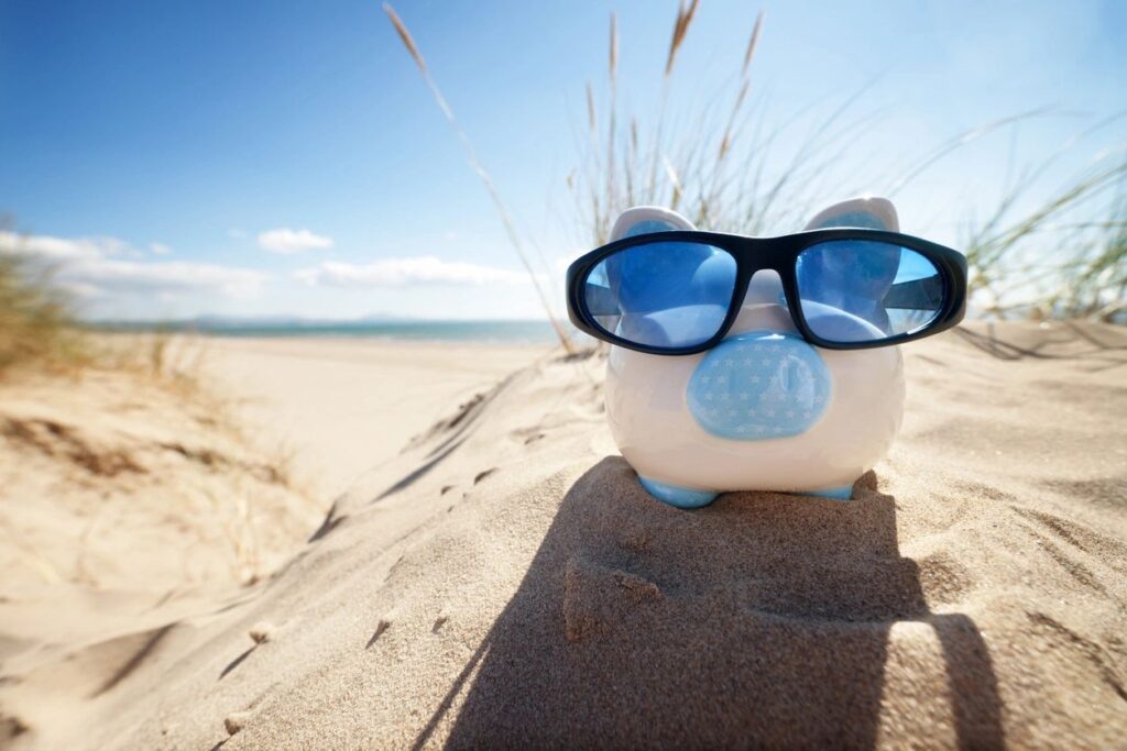 Piggy bank with sunglasses on sandy beach.