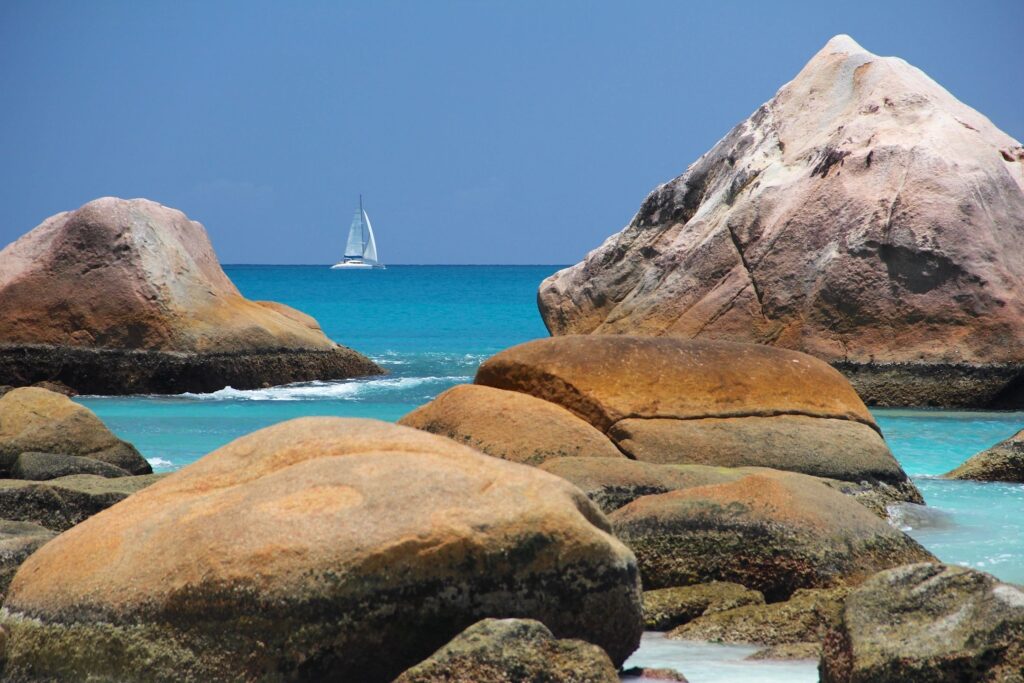 Sailboat on turquoise sea with rocky foreground.